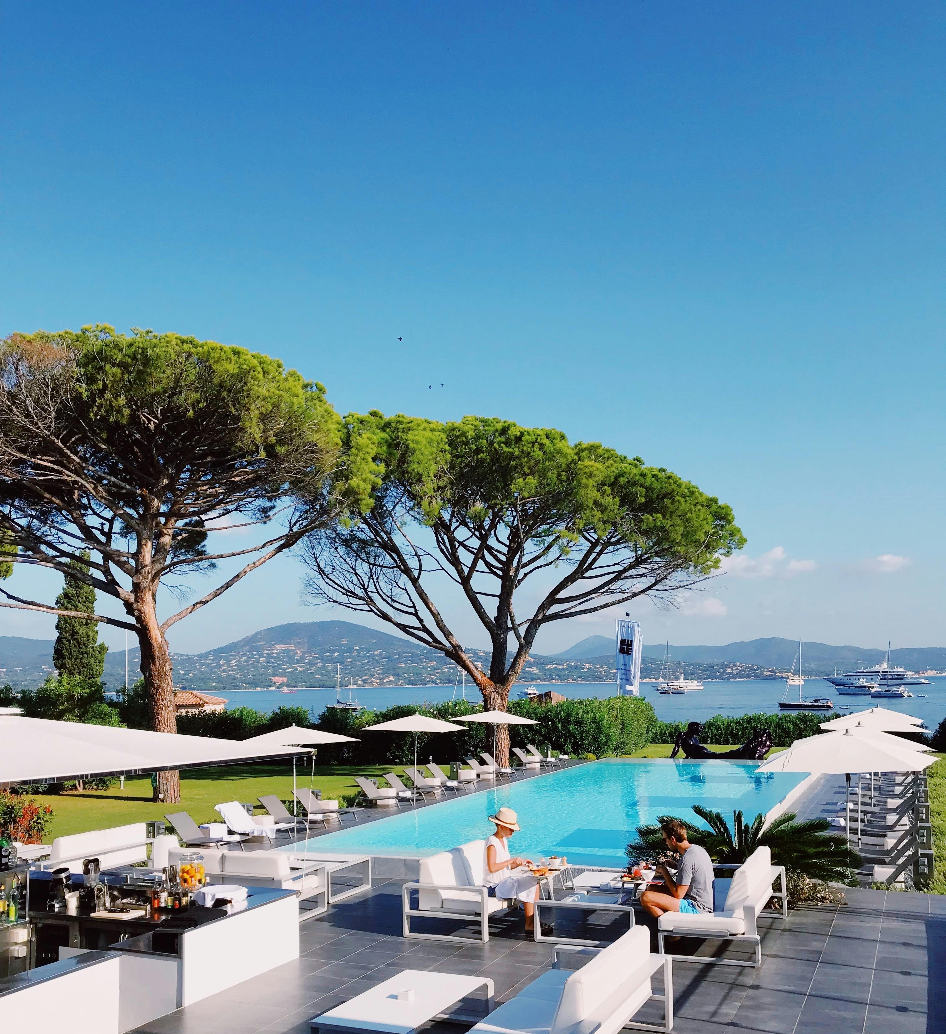 Vista de hotel de luxo com piscina rodeada por cadeiras de banho e uma área verde bela e agrádavel